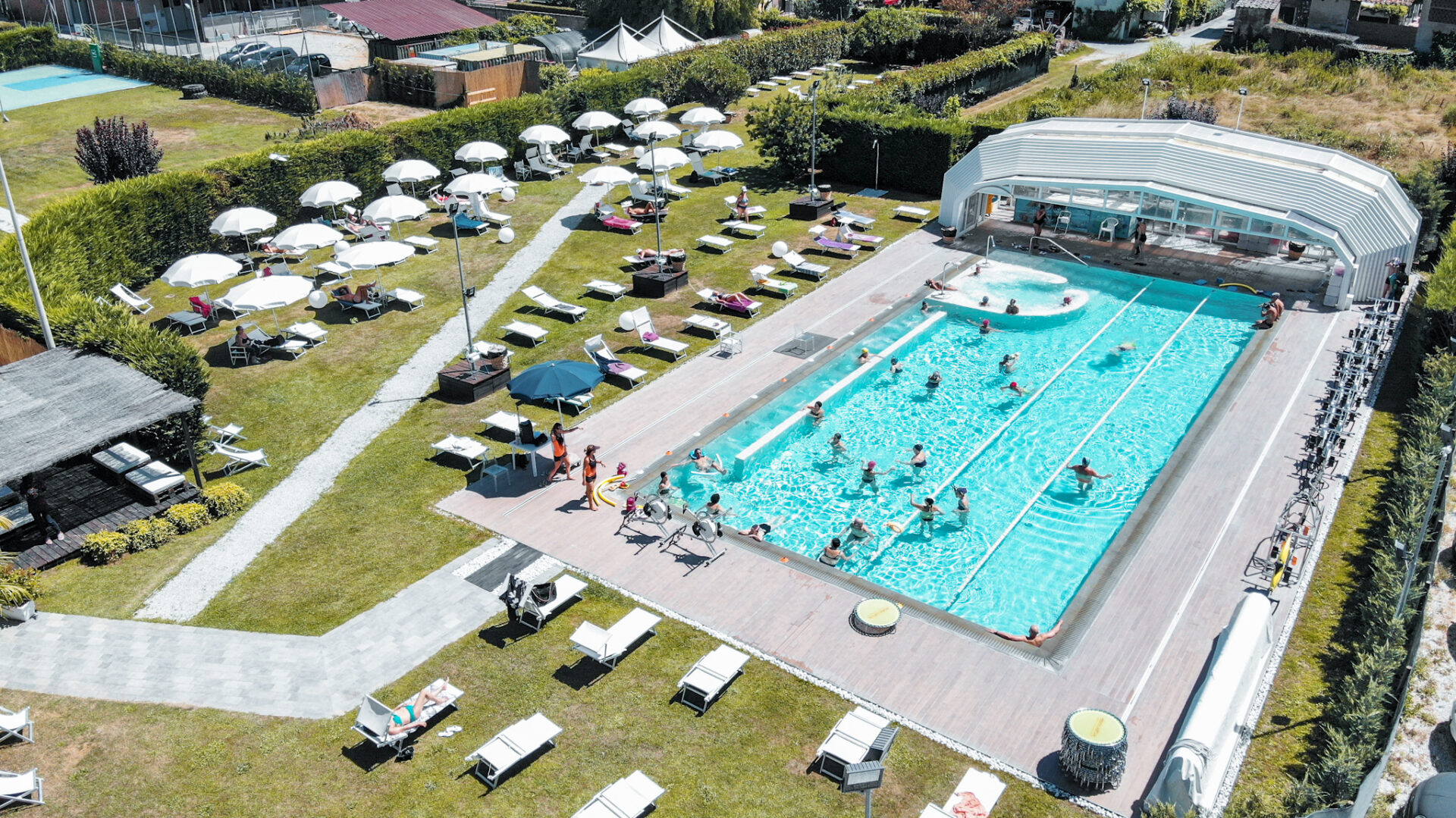 Vista aerea di una piscina all'aperto con lettini, ombrelloni e area verde circostante.