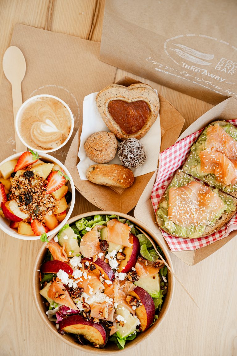 Colazione con caffè, frutta, insalata con salmone e fette di pane integrale.
