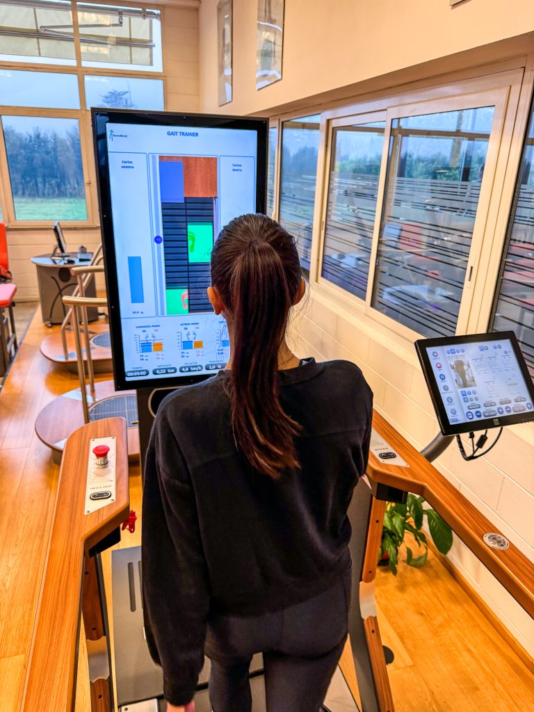 A person walks on a treadmill in a gym, with a large digital screen displaying workout data and graphs.