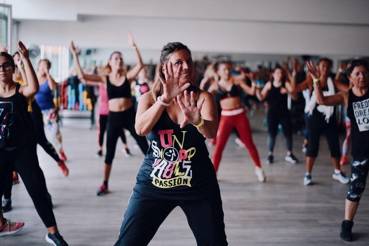 Classe di danza fitness energetica in corso con partecipanti che seguono l'istruttrice in palestra.