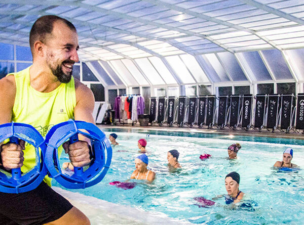 Istruttore in piscina con attrezzi per acquagym, guidando un gruppo di partecipanti in allenamento acquatico.