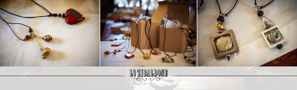 Collane artigianali con ciondoli unici su sfondo beige e marchio Lo Zibaldone.