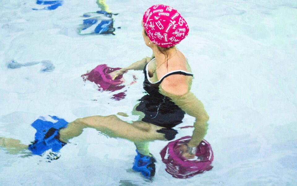 Donna in piscina durante esercizi con attrezzi acquatici per la forza.