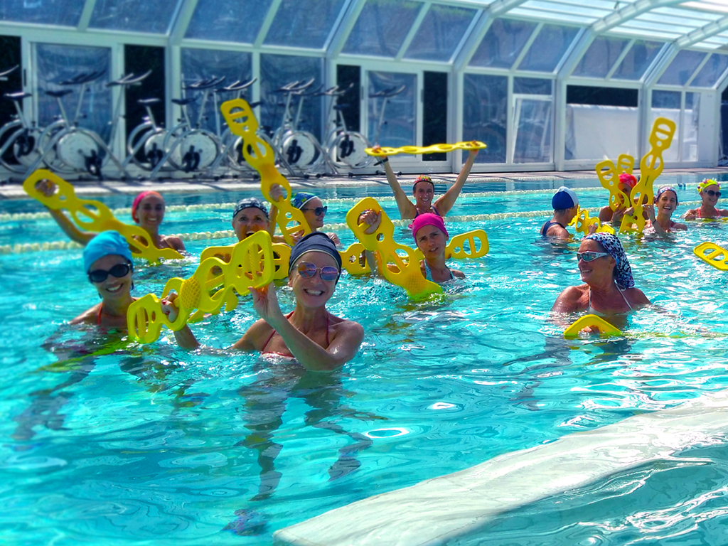 Gruppo di persone in piscina che partecipa a una lezione di acqua fitness, utilizzando attrezzi galleggianti gialli.