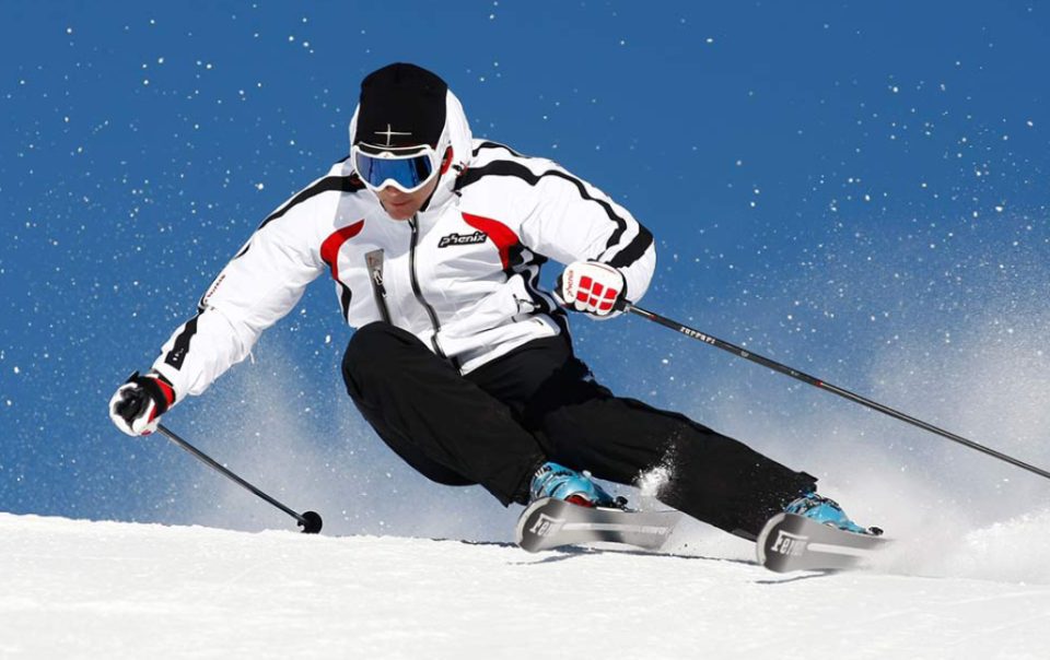 Sciare in pista, atleta con giacca bianca e sci, neve e cielo azzurro.