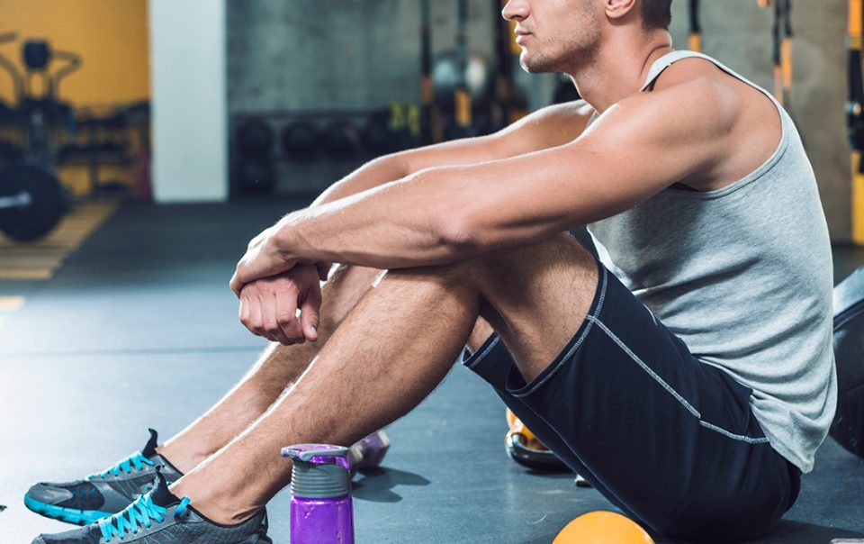 Uomo in palestra seduto a terra in pausa tra gli esercizi.