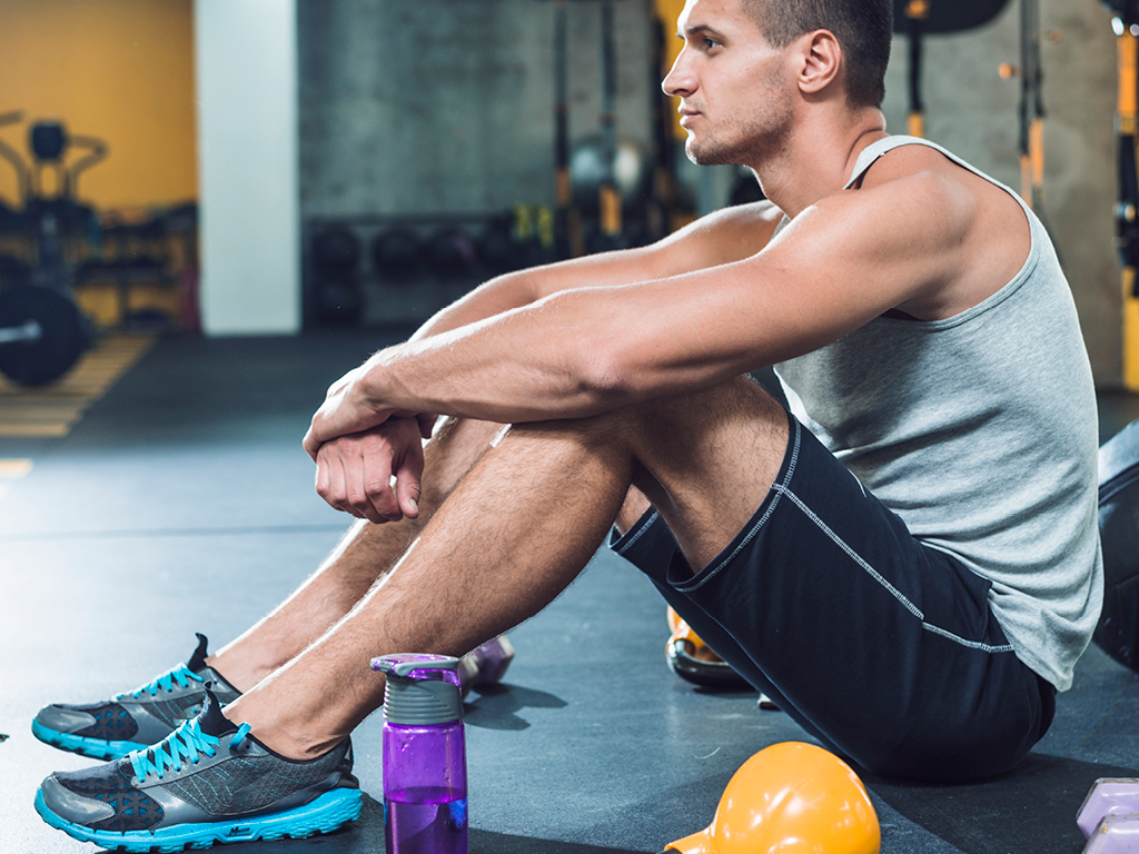 Uomo in palestra seduto a terra in pausa tra gli esercizi.