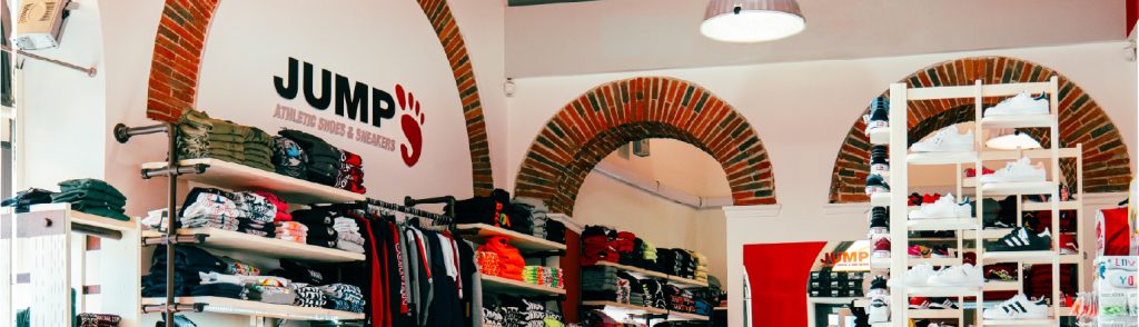 Negozio Jump con abbigliamento sportivo e sneakers, scaffali pieni di prodotti sotto archi in mattoni.