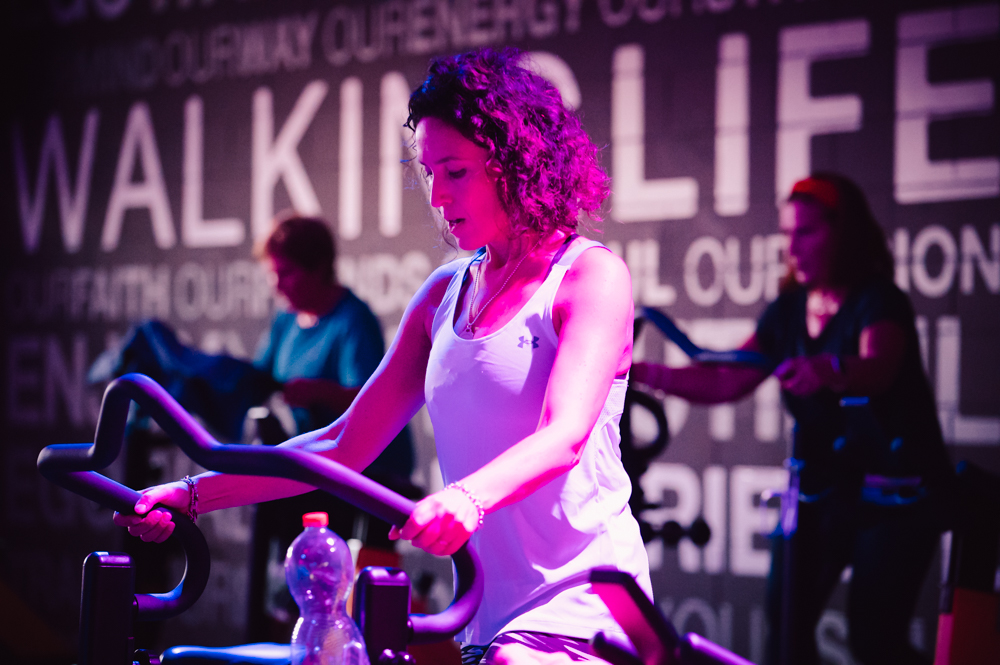 Donna concentrata in una sessione di indoor cycling con luce ambientale in palestra.