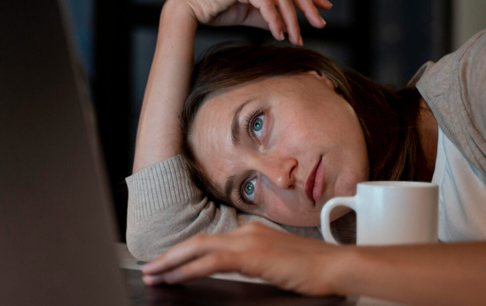 Donna stanca davanti al laptop con una tazza di caffè in mano